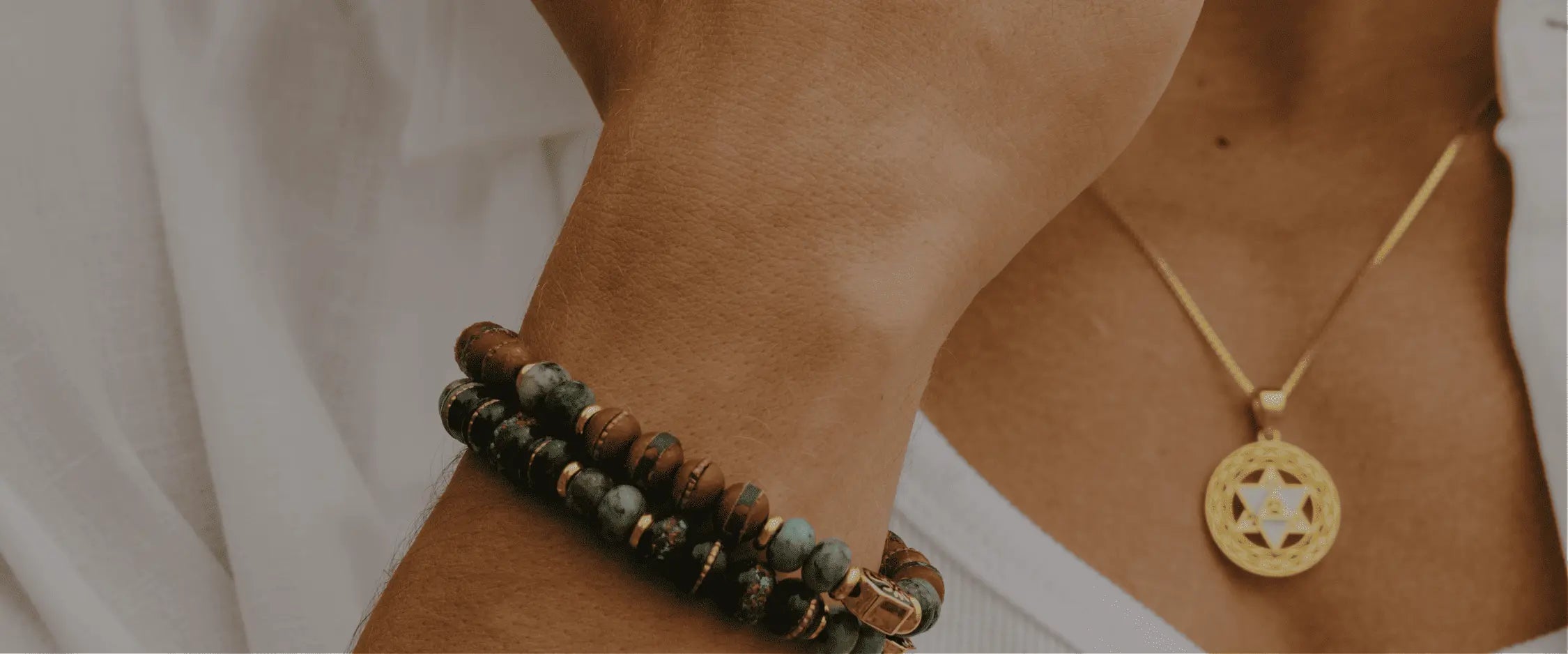 Close-up of a person wearing a gold necklace and a bracelet on a plain background